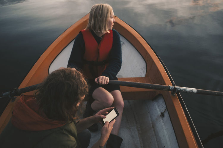 Woman rowing boat while man using mobile phone on lake