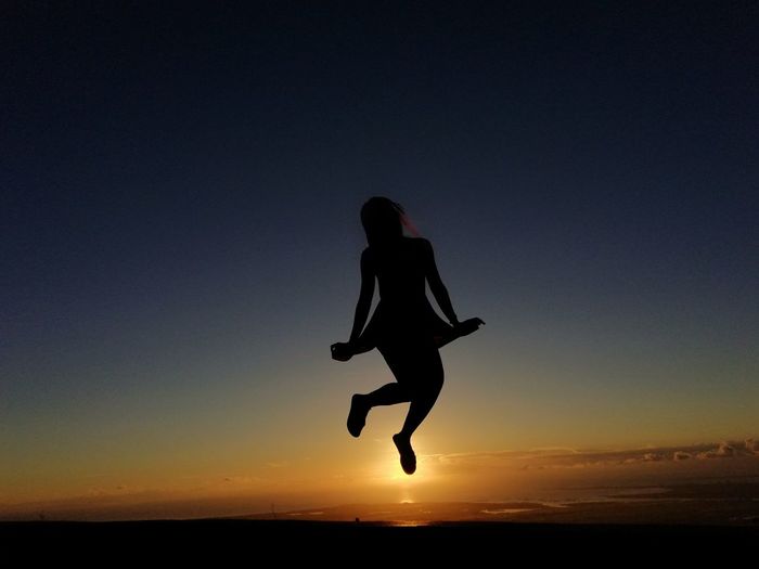 Silhouette woman jumping against sky during sunset
