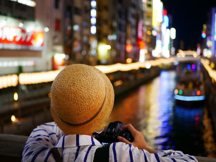 Rear view of woman photographing illuminated boat in city at night