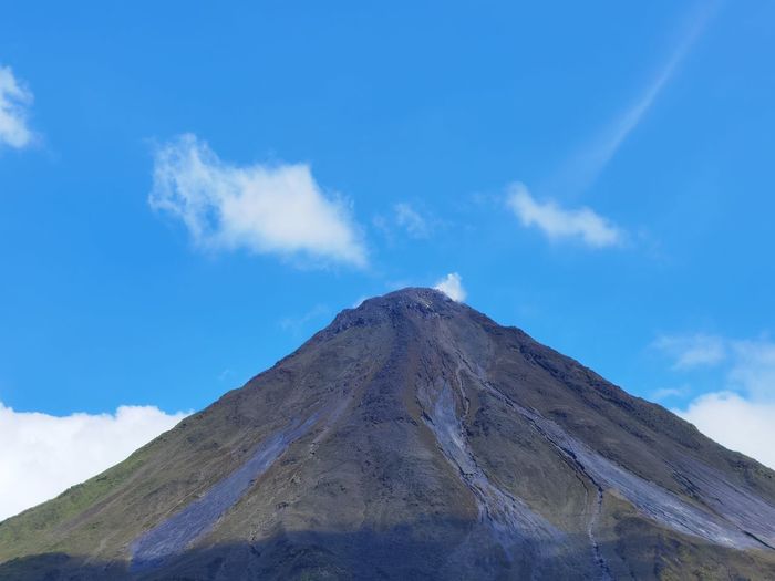 Low angle view of volcanic mountain against blue sky
