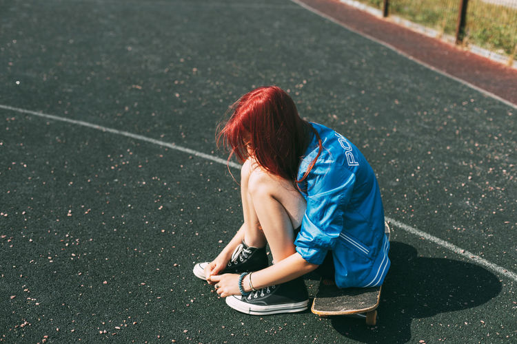 Cute teen girl sitting on a skateboard in the afternoon, outdoors