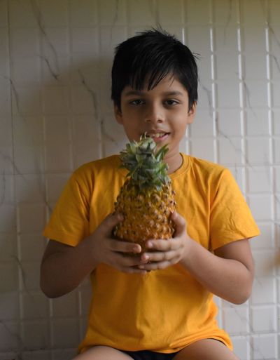 Portrait of smiling boy holding pineapple against wall