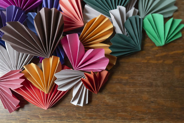 Many colored origami paper valentine hearts arranged on wooden surface