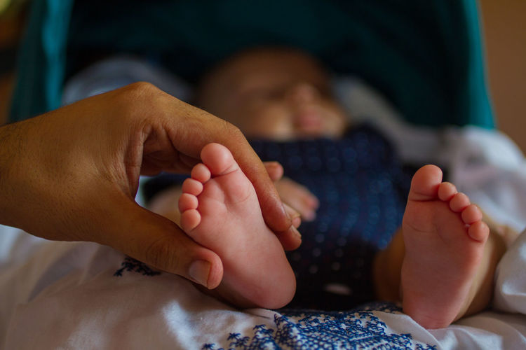 Cropped mother hand holding baby leg on bed at home