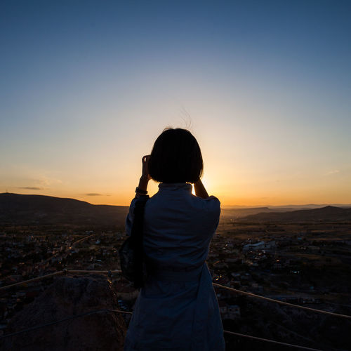 Rear view of woman standing at observation point against clear sky at sunset