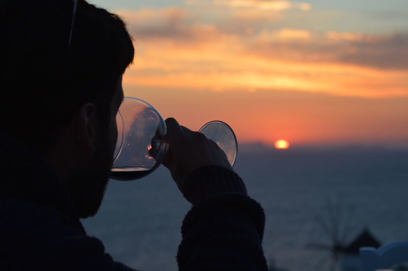 Close-up of man holding sunglasses against sky during sunset