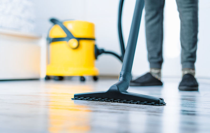 Person cleaning floor with yellow vacuum at home