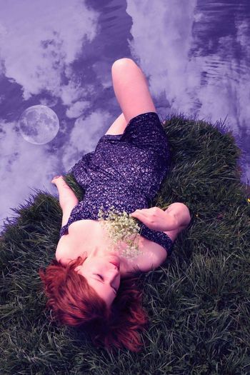 Young woman lying on grass by lake with reflection