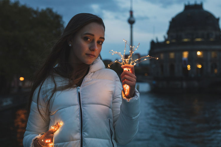 Portrait of young woman holding illuminated lights with fernsehturm in background
