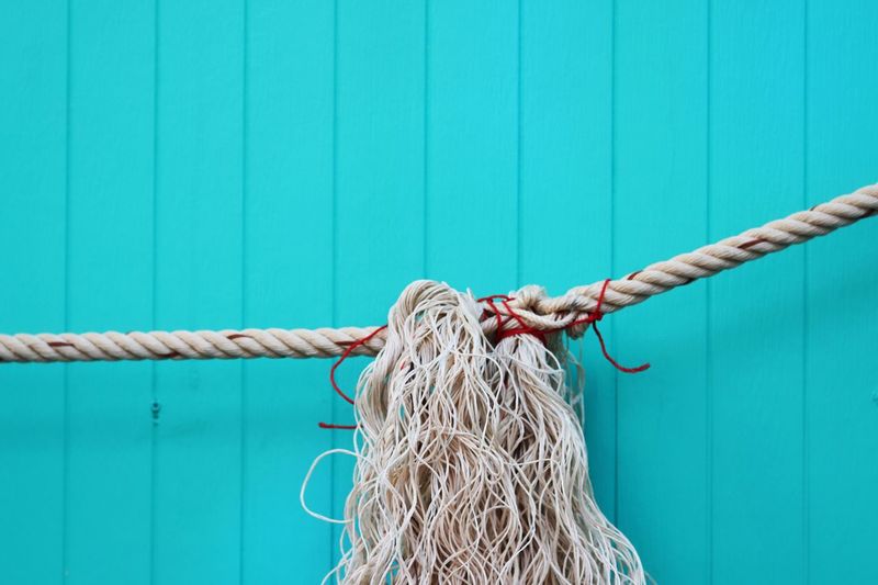 Close-up of rope tied against turquoise wall