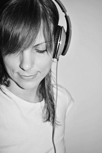 Close-up of woman listening to music through headphones against wall