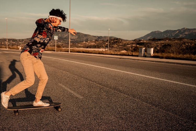 Man skateboarding on road against sky in city