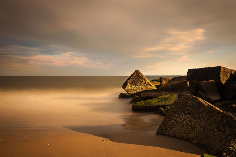 Rock formations on beach against cloudy sky at sunrise