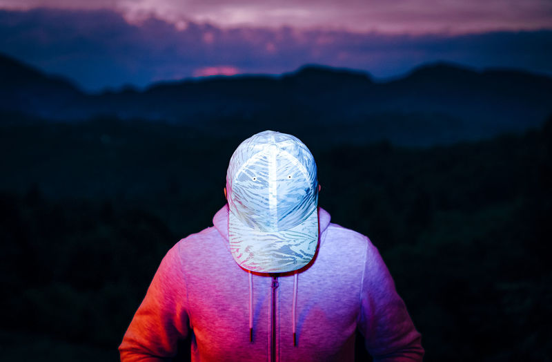 Man with fluorescent baseball cap against mountain at sunset