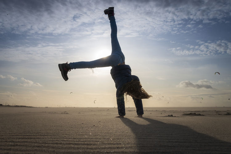Full length of woman jumping on beach against sky during sunset