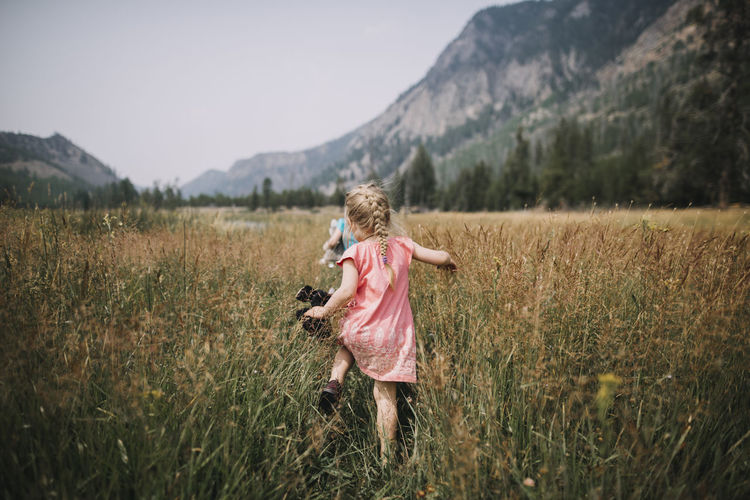 Rear view of carefree girl walking amidst grassy field against mountains at yellowstone national park