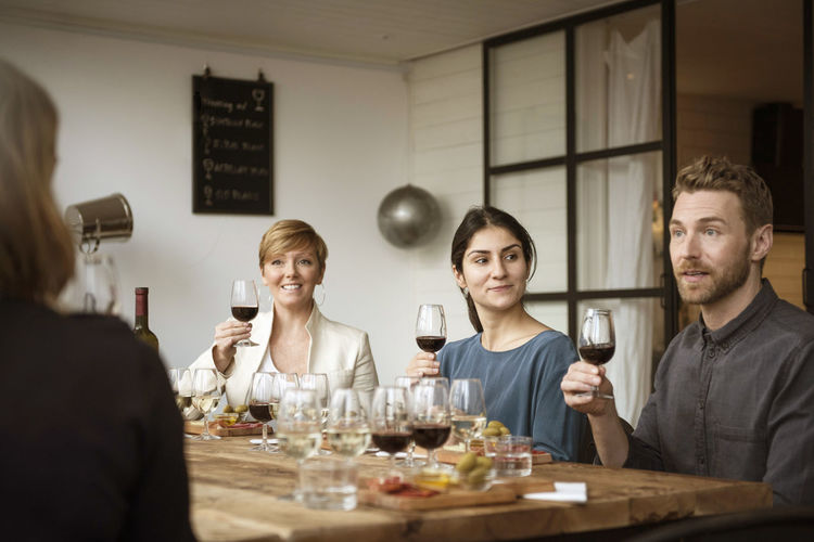 Smiling business people holding wineglass while sitting at table