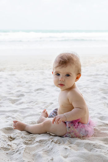 Candid portrait of adorable little baby girl on sand at beach on background of sea. 