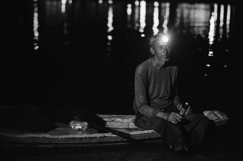 Man sitting on boat in river at night