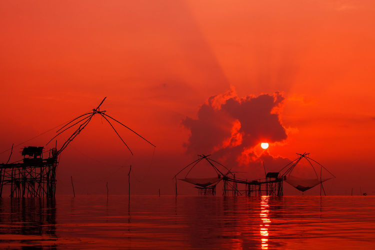 Silhouette chinese fishing net at sea against orange sky during sunset