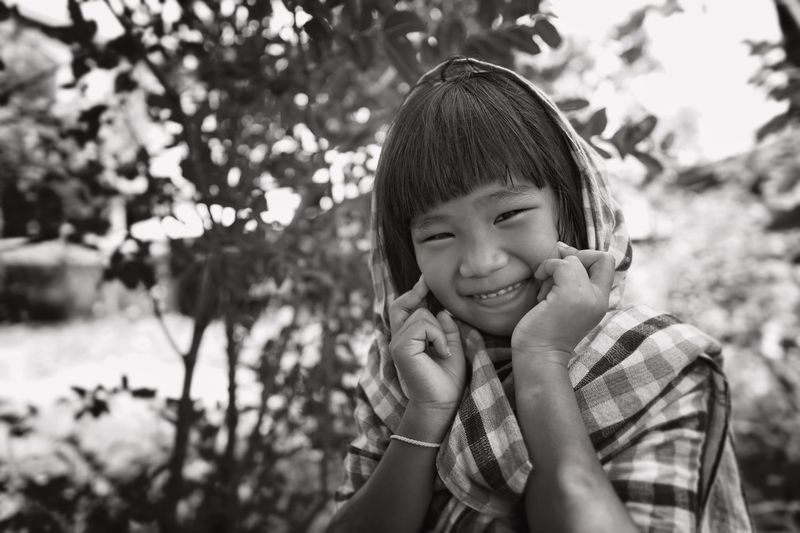 Portrait of smiling girl touching cheek against trees