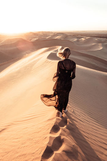 Rear view of woman walking on sand dune at desert