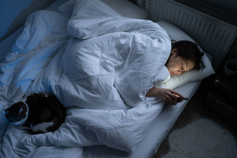 Lonely depressed woman spend night with smartphone sleepless in bed with cat from depression, apathy