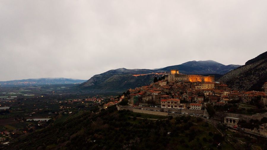 Aerial view of houses on mountains against cloudy sky during sunrise