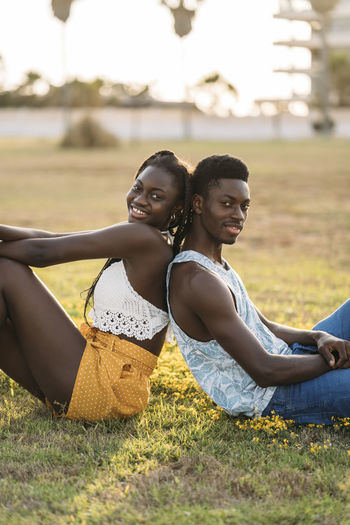 Smiling couple leaning while sitting back to back at grass area