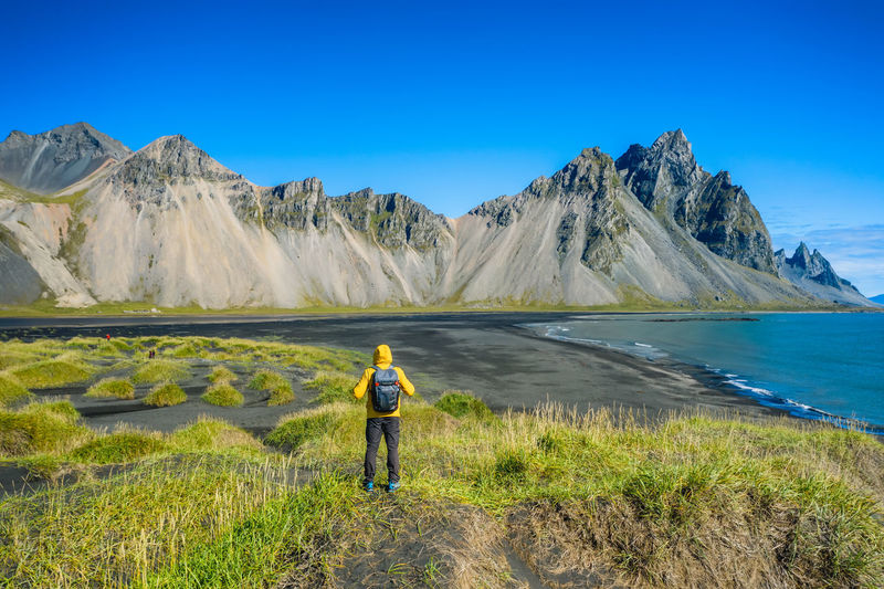 Man hiker with backpack at black sand dunes on the stokksnes icelandic coast with vestrahorn.