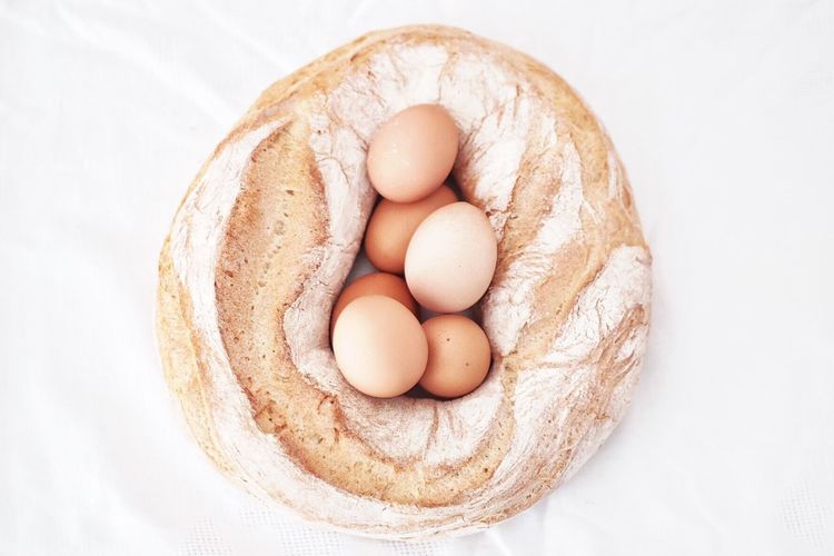 Directly above view of brown eggs and bread on white background