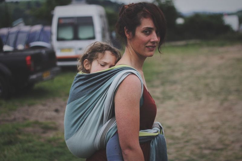 Portrait of woman carrying daughter in fabric on field