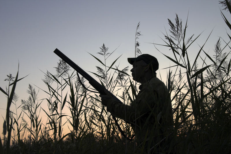 Side view of silhouette hunter holding gun standing against sky