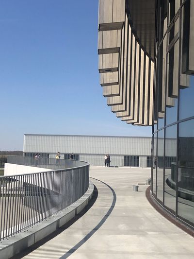 People walking on modern building against clear blue sky