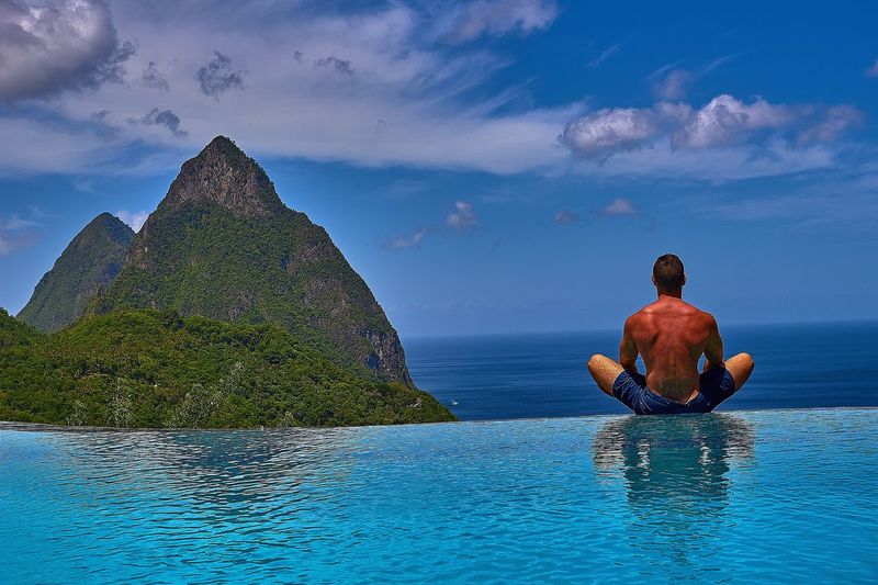 Rear view of shirtless man relaxing by infinity pool against sea