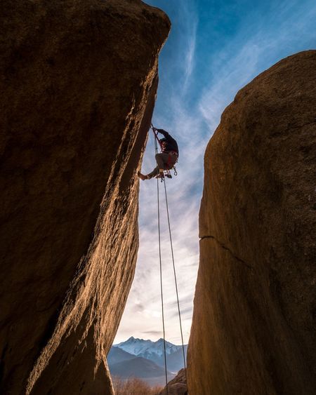 Low angle view of man climbing on rock against sky