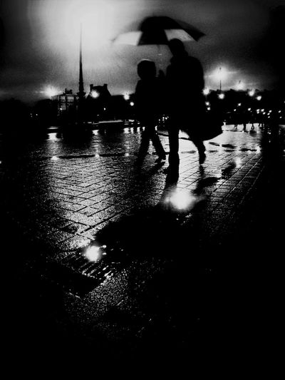 Silhouette people standing on wet illuminated street against sky at night