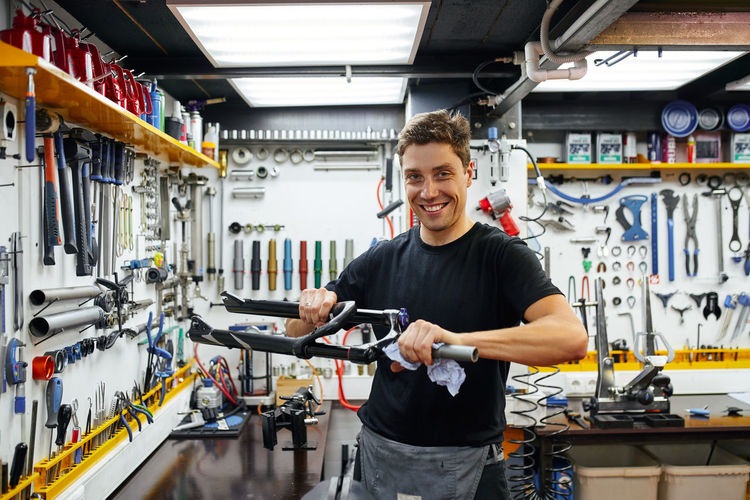 Focused male master wiping bike frame with rag while working in modern repair workshop looking at camera