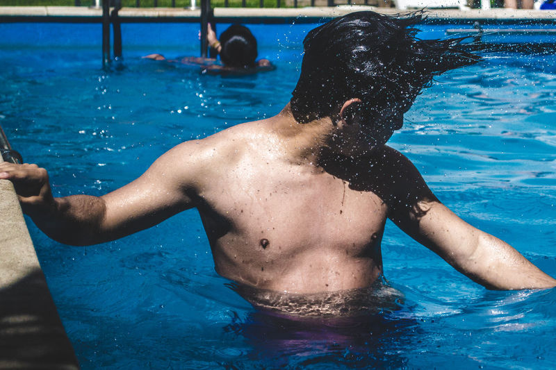 Shirtless young man splashing water in swimming pool