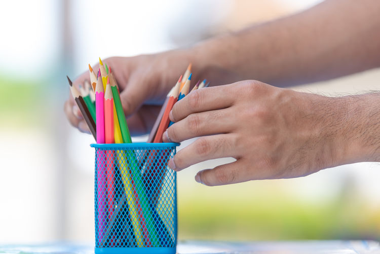 Cropped hands holding colored pencils in desk organizer