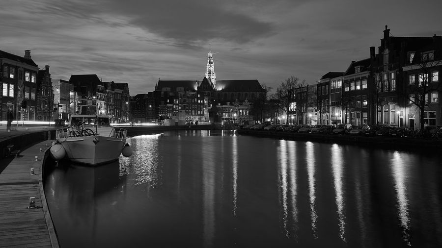 Illuminated grote kerk with reflection in spaarne river against sky at night