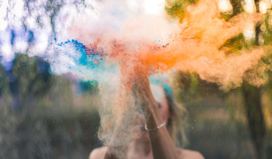 Close-up of woman splashing powder paints against trees