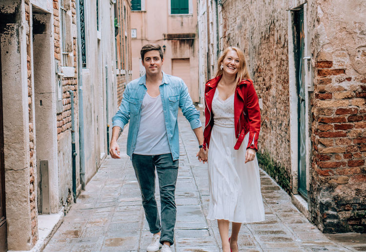 Portrait of young couple holding hands while walking in alley