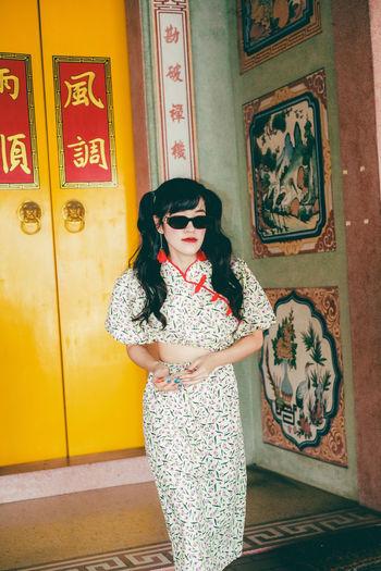 Portrait of woman in yellow modern cheongsam holding a red envelope at chinese temple 