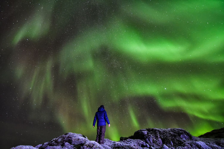 Rear view of person standing on rock against northern lights at night