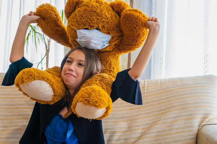 Girl carrying teddy bear on shoulders at home