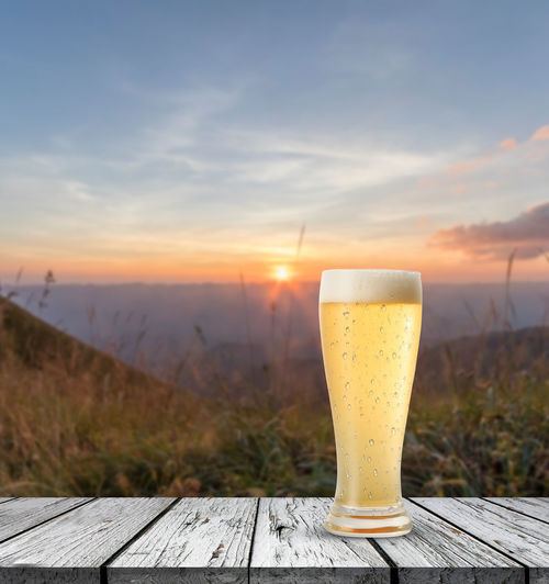 Beer glass on table against sky during sunset