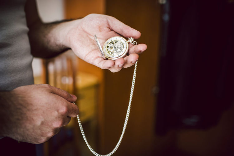 Midsection of man holding pocket watch at home