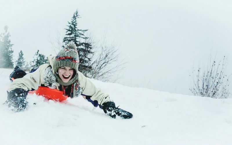 Happy young woman sledding on snowcapped mountain during winter