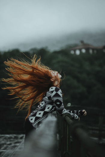 Side view of redhead woman tossing hair while leaning on railing